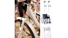 Po prawej stronie biały rower po lewej od góry kule, wózek inwalidzki,chodzik
